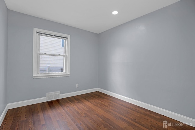 empty room with dark wood-style floors, recessed lighting, visible vents, and baseboards