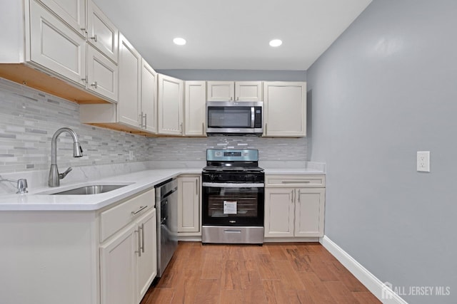 kitchen featuring stainless steel appliances, light countertops, light wood-style flooring, a sink, and baseboards