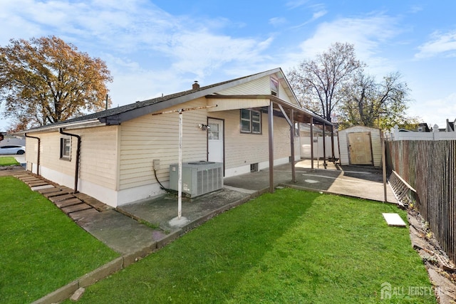 rear view of house with a fenced backyard, a storage unit, a yard, a patio area, and central AC