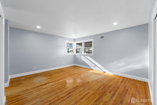 empty room with wood finished floors, visible vents, and baseboards