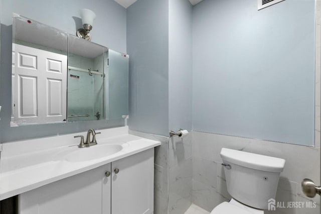 full bath featuring a stall shower, tile walls, vanity, and toilet