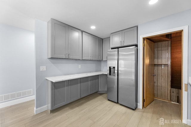 kitchen with light wood-type flooring, gray cabinets, visible vents, and stainless steel refrigerator with ice dispenser