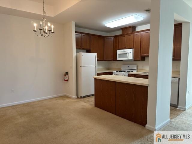 kitchen featuring light carpet, white appliances, an inviting chandelier, and hanging light fixtures