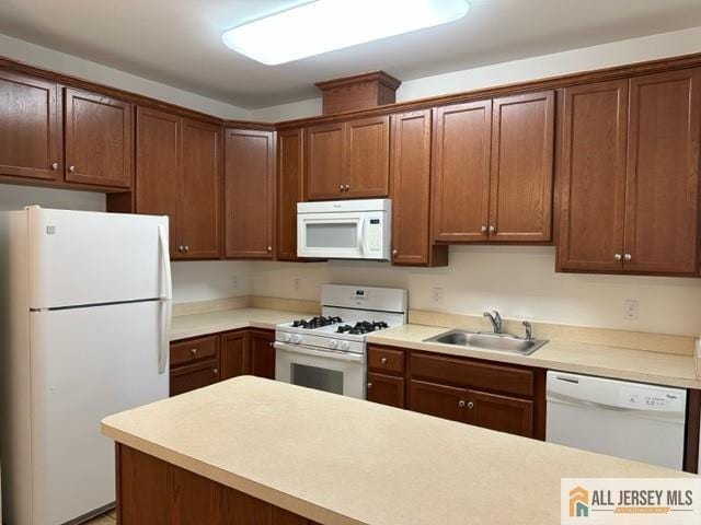 kitchen with a sink, white appliances, brown cabinetry, and light countertops