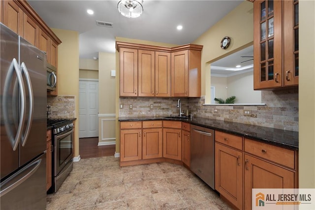 704 Schindler Dr, South Brunswick, NJ 08852 - kitchen with appliances with stainless steel finishes, decorative backsplash, brown cabinetry, dark stone countertops, and glass insert cabinets