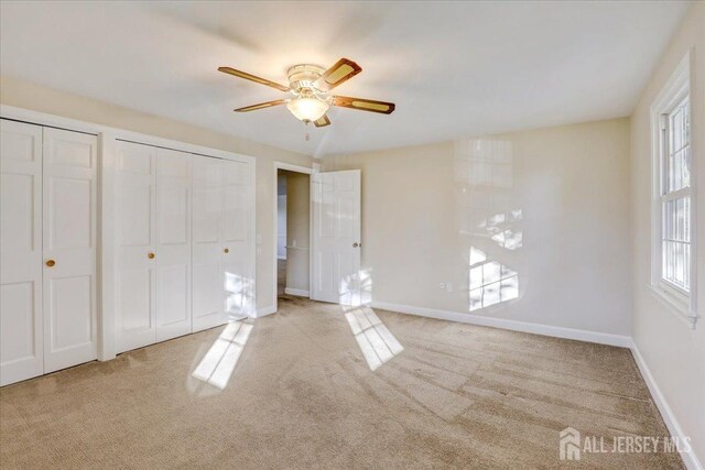 unfurnished bedroom with light carpet, two closets, and ceiling fan