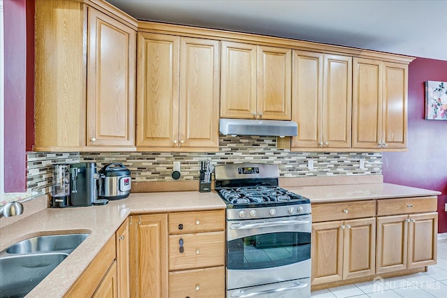 kitchen with stainless steel gas range, a sink, decorative backsplash, light countertops, and under cabinet range hood