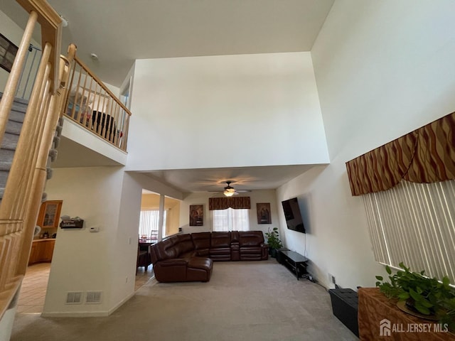 carpeted living room featuring a towering ceiling and ceiling fan