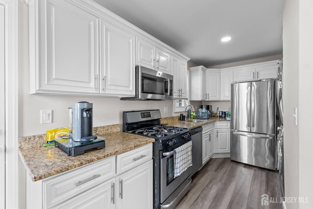 kitchen featuring white cabinetry, hardwood / wood-style flooring, light stone countertops, sink, and appliances with stainless steel finishes