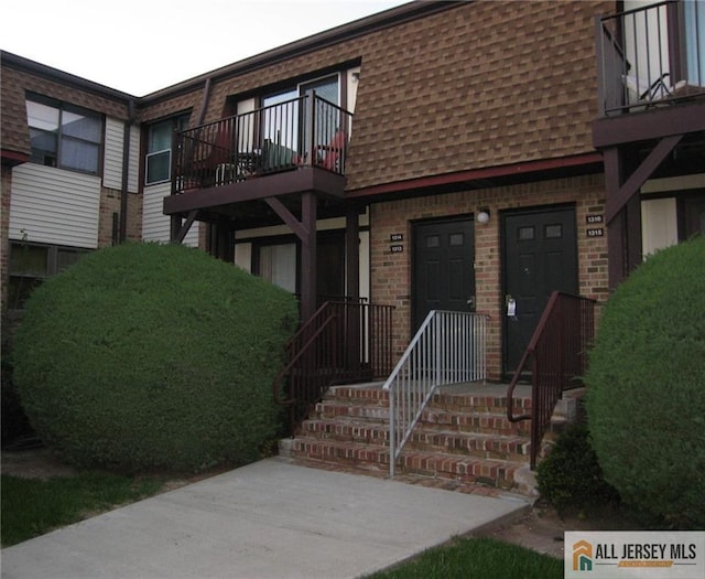 exterior space featuring brick siding, a shingled roof, and a balcony