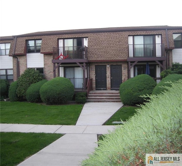 view of front of house with brick siding, a balcony, and a front yard
