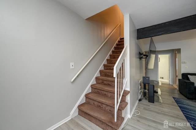 staircase with beam ceiling, visible vents, baseboards, and wood finished floors