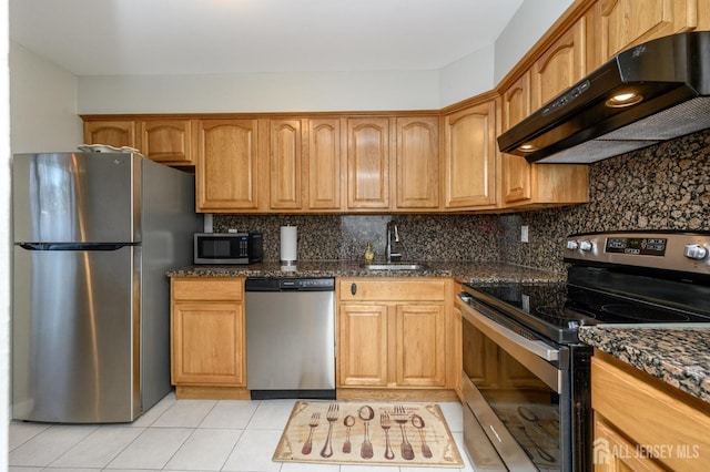 kitchen featuring under cabinet range hood, stainless steel appliances, a sink, backsplash, and dark stone counters