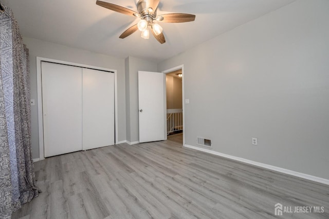 unfurnished bedroom with a closet, visible vents, ceiling fan, wood finished floors, and baseboards