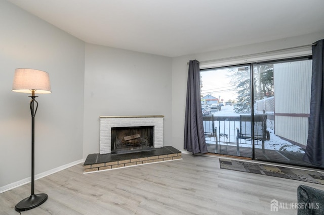 unfurnished living room featuring a brick fireplace, baseboards, and wood finished floors