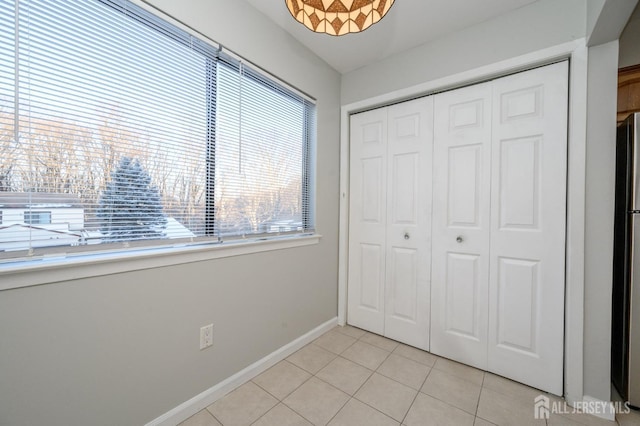 unfurnished bedroom featuring light tile patterned floors, baseboards, a closet, and freestanding refrigerator