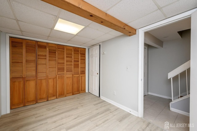 interior space with light wood-type flooring, a paneled ceiling, a closet, and baseboards