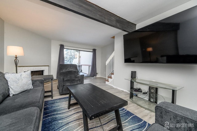 living room featuring baseboards, lofted ceiling with beams, stairway, wood finished floors, and a brick fireplace