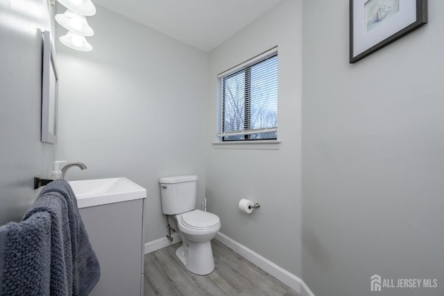 half bathroom featuring wood finished floors, vanity, toilet, and baseboards