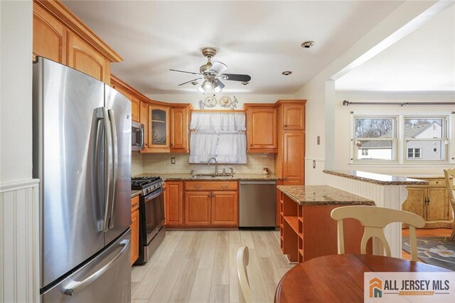 kitchen with light stone counters, light hardwood / wood-style flooring, stainless steel appliances, ceiling fan, and sink