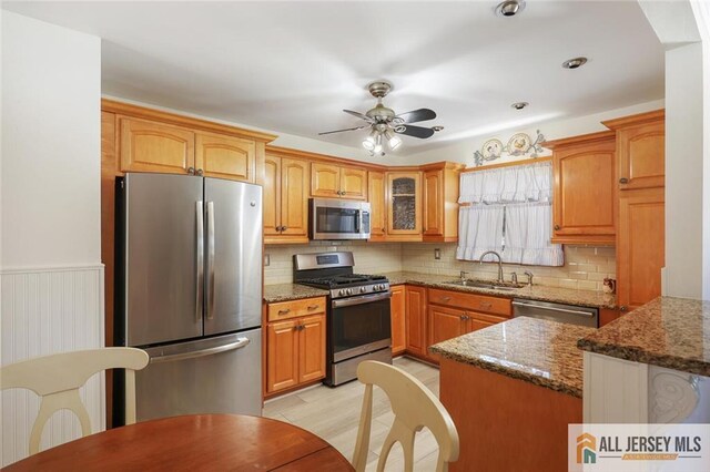 kitchen featuring stainless steel appliances, dark stone counters, ceiling fan, sink, and light hardwood / wood-style flooring