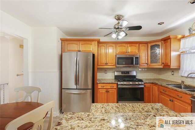 kitchen with appliances with stainless steel finishes, ceiling fan, sink, and tasteful backsplash