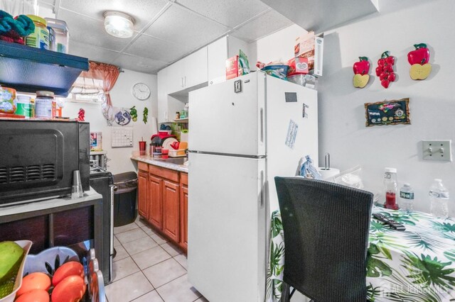 184 Seaman St, New Brunswick, NJ 08901 - kitchen featuring freestanding refrigerator, a paneled ceiling, light countertops, light tile patterned flooring, and brown cabinetry