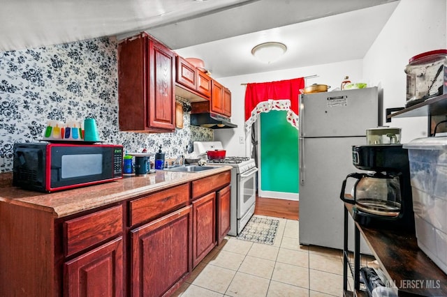 184 Seaman St, New Brunswick, NJ 08901 - kitchen with white appliances, under cabinet range hood, light tile patterned floors, wallpapered walls, and reddish brown cabinets