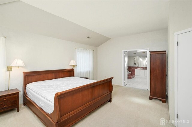 carpeted bedroom with ensuite bathroom and lofted ceiling