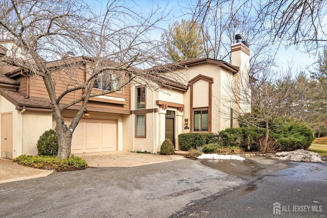 view of front of home with a garage, a chimney, aphalt driveway, and stucco siding