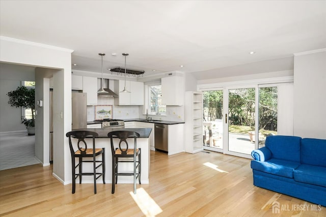 kitchen with decorative light fixtures, white cabinetry, sink, stainless steel appliances, and wall chimney range hood