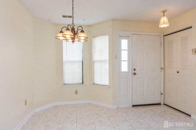 foyer entrance featuring a textured ceiling, an inviting chandelier, and light tile patterned flooring