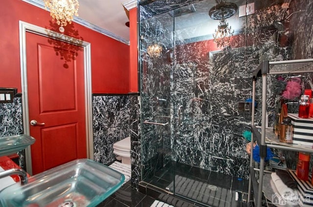 bathroom with tile walls, a shower stall, a sink, toilet, and ornamental molding