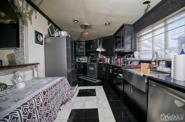 kitchen with exhaust hood, dark cabinets, appliances with stainless steel finishes, and dark tile patterned flooring
