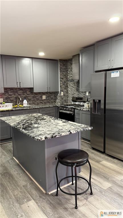 kitchen with a sink, wall chimney exhaust hood, stainless steel appliances, dark stone counters, and gray cabinets