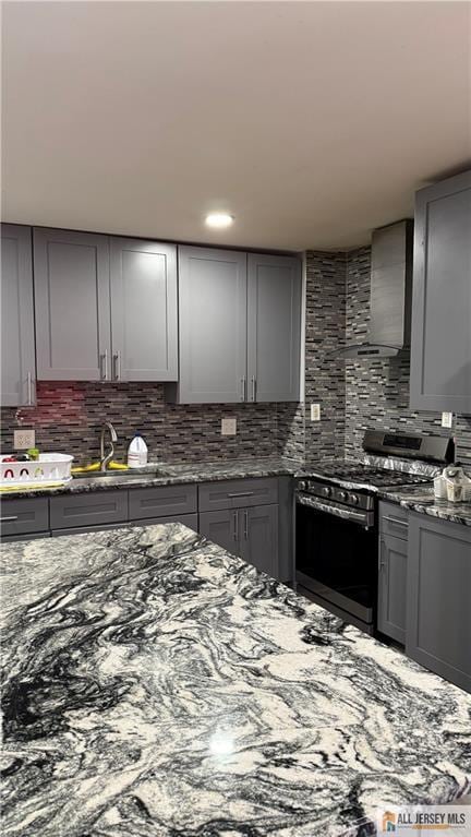 kitchen featuring wall chimney range hood, gray cabinets, a sink, and gas range