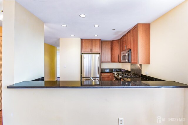 20 Livingston Ave Unit 902, New Brunswick, NJ 08901 - kitchen with stainless steel appliances, a peninsula, recessed lighting, dark countertops, and brown cabinetry