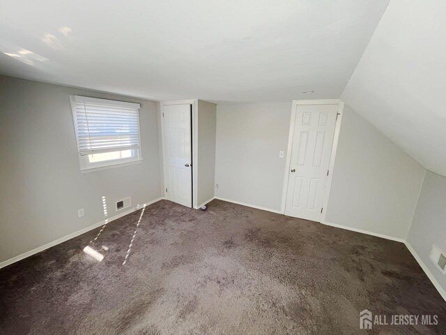 interior space featuring vaulted ceiling and dark carpet