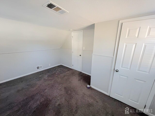 bonus room featuring lofted ceiling, dark carpet, and a textured ceiling