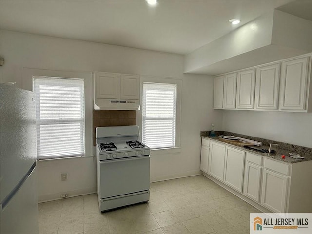 kitchen featuring under cabinet range hood, white gas range oven, white cabinets, and freestanding refrigerator