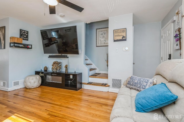 living room featuring ceiling fan, stairs, wood finished floors, and visible vents