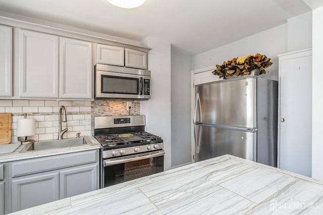 kitchen with a sink, appliances with stainless steel finishes, light stone countertops, and tasteful backsplash