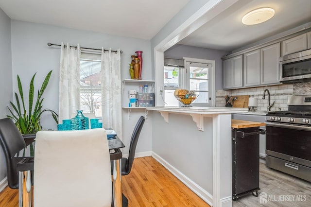 kitchen featuring light wood-style floors, gray cabinets, backsplash, and stainless steel appliances