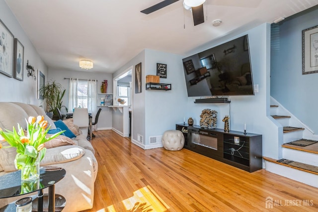living room featuring baseboards, stairs, ceiling fan, and wood finished floors
