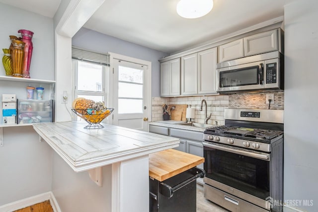 kitchen with appliances with stainless steel finishes, a sink, baseboards, tasteful backsplash, and gray cabinetry