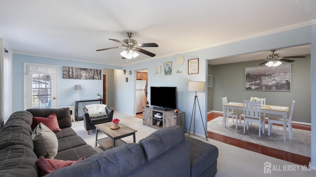 living room featuring ornamental molding, light wood-type flooring, a ceiling fan, and baseboards