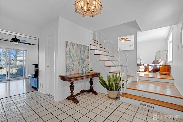 entrance foyer with stairs, visible vents, and ceiling fan with notable chandelier