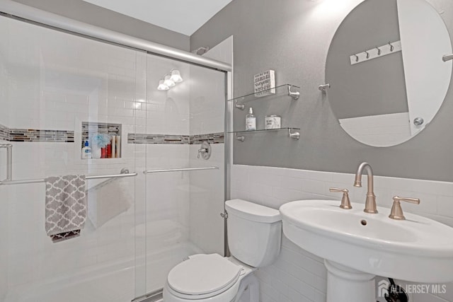 bathroom featuring a stall shower, a sink, tile walls, and toilet