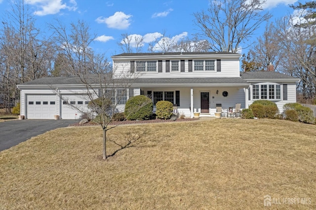 traditional home featuring a chimney, a porch, an attached garage, a front yard, and driveway