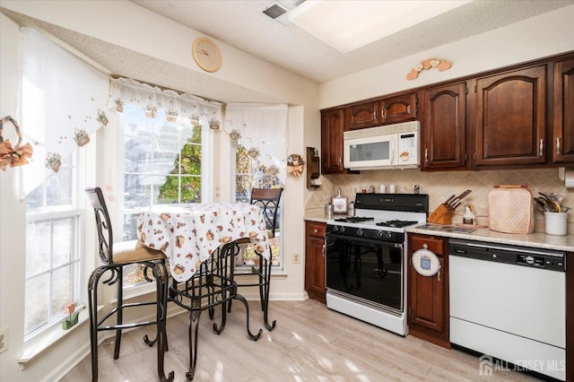 kitchen with decorative backsplash, visible vents, light wood-style floors, light countertops, and white appliances